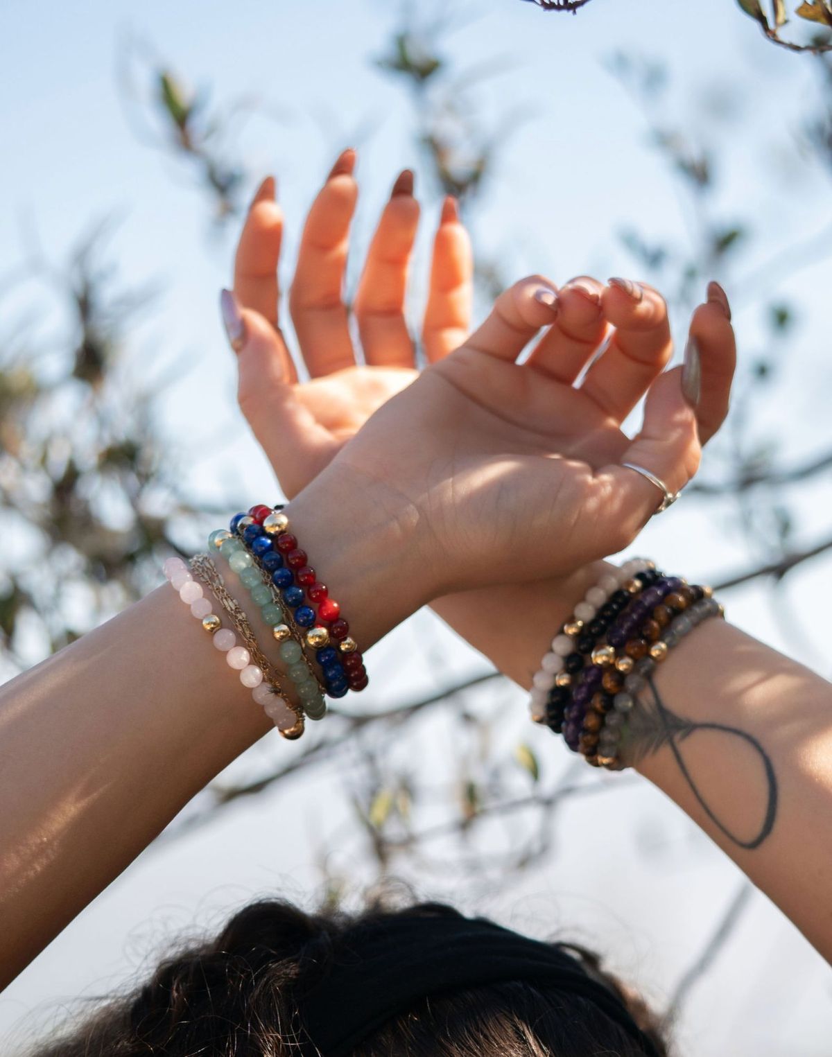Two arms crossed toward the sky, each wearing a stack of crystal and gold bracelets